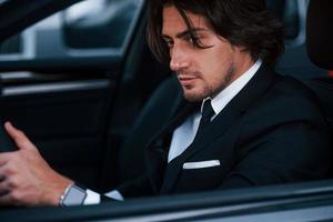 Young businessman in black suit and tie inside modern automobile photo