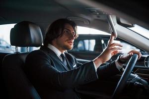 Young businessman in black suit and tie driving modern automobile photo