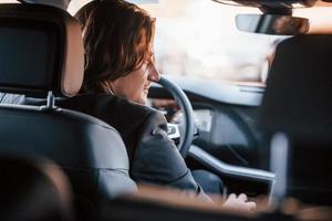 Young businessman in black suit and tie driving modern automobile photo