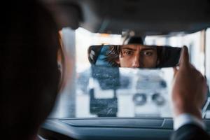 Young businessman in black suit and tie driving modern automobile photo