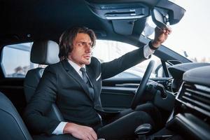 Young businessman in black suit and tie driving modern automobile photo