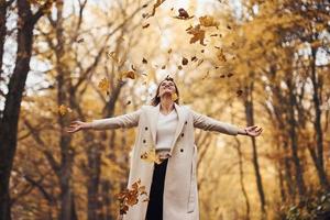 Having fun with leaves. Portrait of young brunette that is in autumn forest at daytime photo