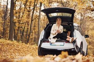 Girl sits on the back of car. Modern brand new automobile in the forest photo