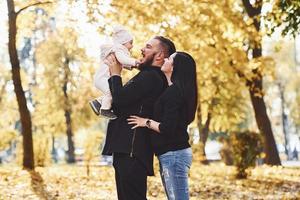 Cheerful family having fun together with their child in beautiful autumn park photo