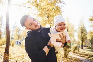 Nice sunlight. Father in casual clothes with his child is in the beautiful autumn park photo