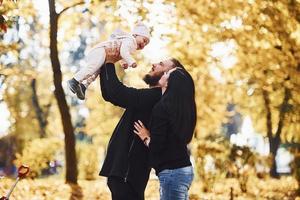 Cheerful family having fun together with their child in beautiful autumn park photo