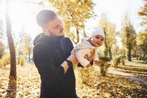 Nice sunlight. Father in casual clothes with his child is in the beautiful autumn park photo