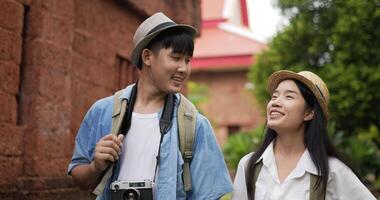 Closeup of Happy asian traveler couple with hat hand together while visiting at ancient temple. Smiling young man and woman walking and looking ancient temple. Holiday, travel and hobby concept. video
