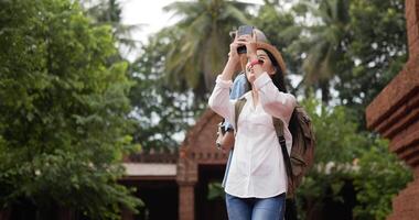 Happy asian traveler couple with hat takes a photo and visits ancient temple. Smiling young man and woman standing and looking ancient temple. Holiday, travel and hobby concept. video