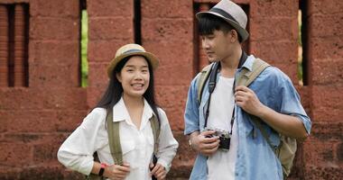 Portrait of asian traveler couple with hat talking and looking at camera at ancient temple. Smiling young man and woman videoblogger filming new vlog video with professional camera at ancient temple.