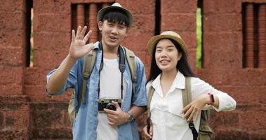 Portrait of asian traveler couple with hat talking and looking at camera at ancient temple. Smiling young man and woman videoblogger filming new vlog video with professional camera at ancient temple.