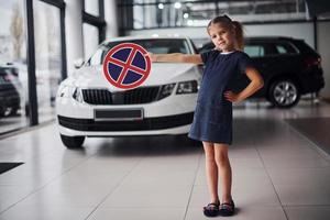 Portrait of cute little girl that holds road sign in hands in automobile salon photo