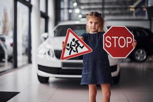 Portrait of cute little girl that holds road signs in hands in automobile salon photo