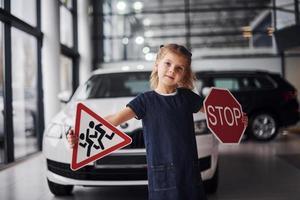 Portrait of cute little girl that holds road signs in hands in automobile salon photo