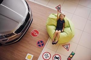 Top view of cute little girl that holds road signs in hands in automobile salon photo