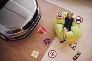 Top view of cute little girl that holds road signs in hands in automobile salon photo