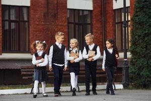 grupo de niños con uniforme escolar que están juntos al aire libre cerca del edificio de educación foto