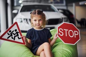 Portrait of cute little girl that holds road signs in hands in automobile salon photo