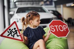 Portrait of cute little girl that holds road signs in hands in automobile salon photo