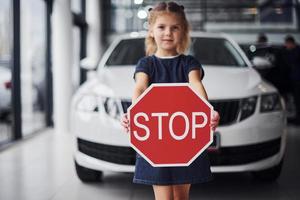 Portrait of cute little girl that holds road sign in hands in automobile salon photo