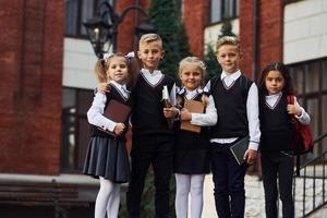 grupo de niños con uniforme escolar que están juntos al aire libre cerca del edificio de educación foto