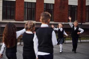 tener una reunión. grupo de niños con uniforme escolar que están juntos al aire libre cerca del edificio de educación