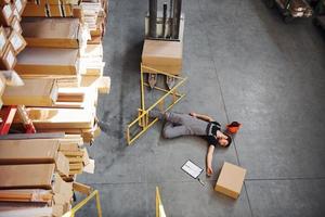 Warehouse worker after an accident in the storage. Man in uniform lying down on the ground photo