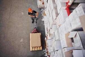 Top view of young male worker in uniform that is in the warehouse pushing pallet truck photo