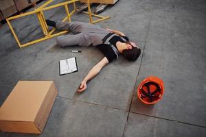 Warehouse worker after an accident in the storage. Man in uniform lying down on the ground photo