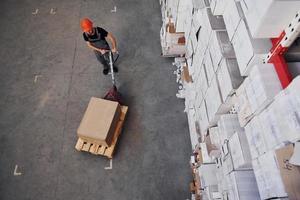 Top view of young male worker in uniform that is in the warehouse pushing pallet truck photo