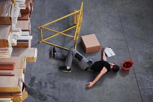 Warehouse worker after an accident in the storage. Man in uniform lying down on the ground photo