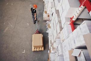 Top view of young male worker in uniform that is in the warehouse pushing pallet truck photo