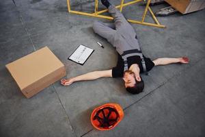 Warehouse worker after an accident in the storage. Man in uniform lying down on the ground photo