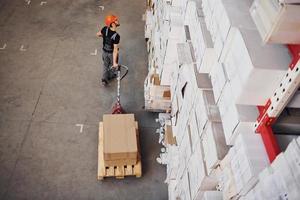 Top view of young male worker in uniform that is in the warehouse pushing pallet truck photo