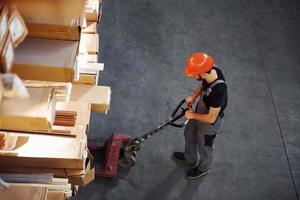 Top view of young male worker in uniform that is in the warehouse pushing pallet truck photo