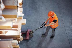 Top view of young male worker in uniform that is in the warehouse pushing pallet truck photo