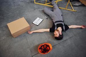 Warehouse worker after an accident in the storage. Man in uniform lying down on the ground photo