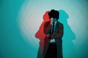 Portrait of young stylish man in hat, suit and tie that stands in neon lights in the studio photo