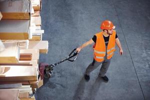 Top view of young male worker in uniform that is in the warehouse pushing pallet truck photo