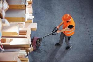 Top view of young male worker in uniform that is in the warehouse pushing pallet truck photo