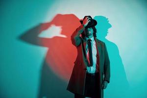 Portrait of young stylish man in hat, suit and tie that stands in neon lights in the studio photo