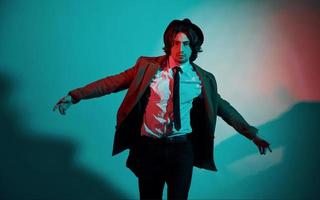 Portrait of young stylish man in hat, suit and tie that stands in neon lights in the studio photo