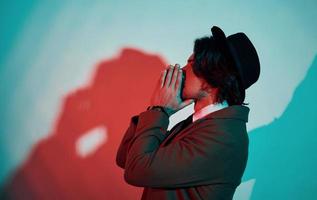 Portrait of young stylish man in hat, suit and tie that stands in neon lights in the studio photo