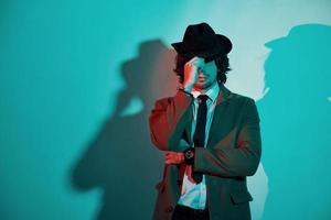 Portrait of young stylish man in hat, suit and tie that stands in neon lights in the studio photo