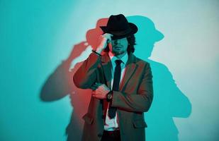 retrato de un joven elegante con sombrero, traje y corbata que se encuentra en luces de neón en el estudio foto