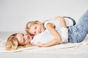 Mother with her daughter together is on the ground in the studio with white background photo