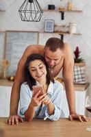 pareja en la cocina a la hora de la mañana con teléfono móvil foto