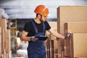 Storage worker in uniform and notepad in hands checks production photo