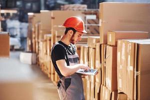 trabajador de almacenamiento en uniforme y portátil moderno en las manos comprueba la producción foto