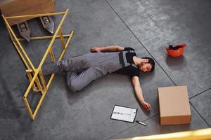 Warehouse worker after an accident in the storage. Man in uniform lying down on the ground photo